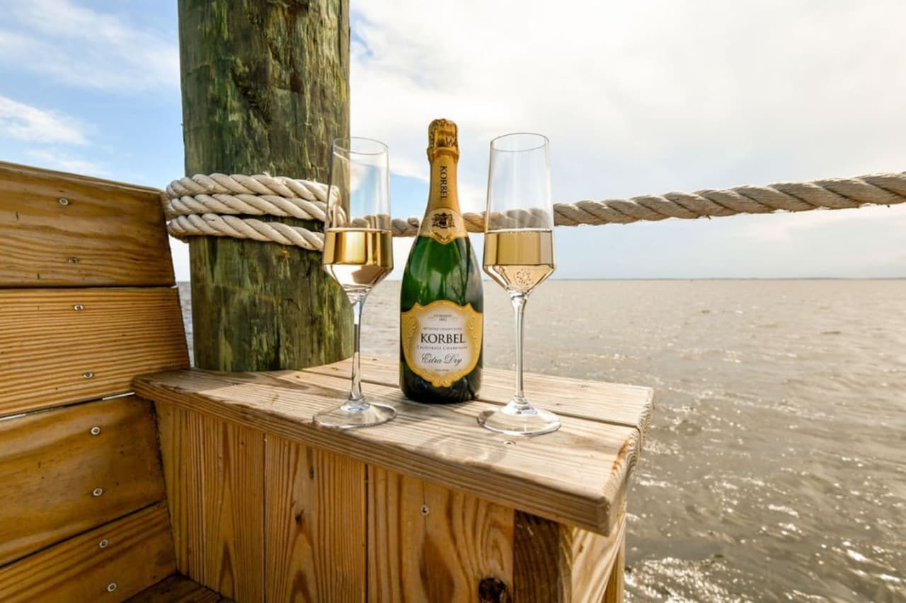 Chilled champagne & glasses set out on the dock railing w/ calm sound water beyond.