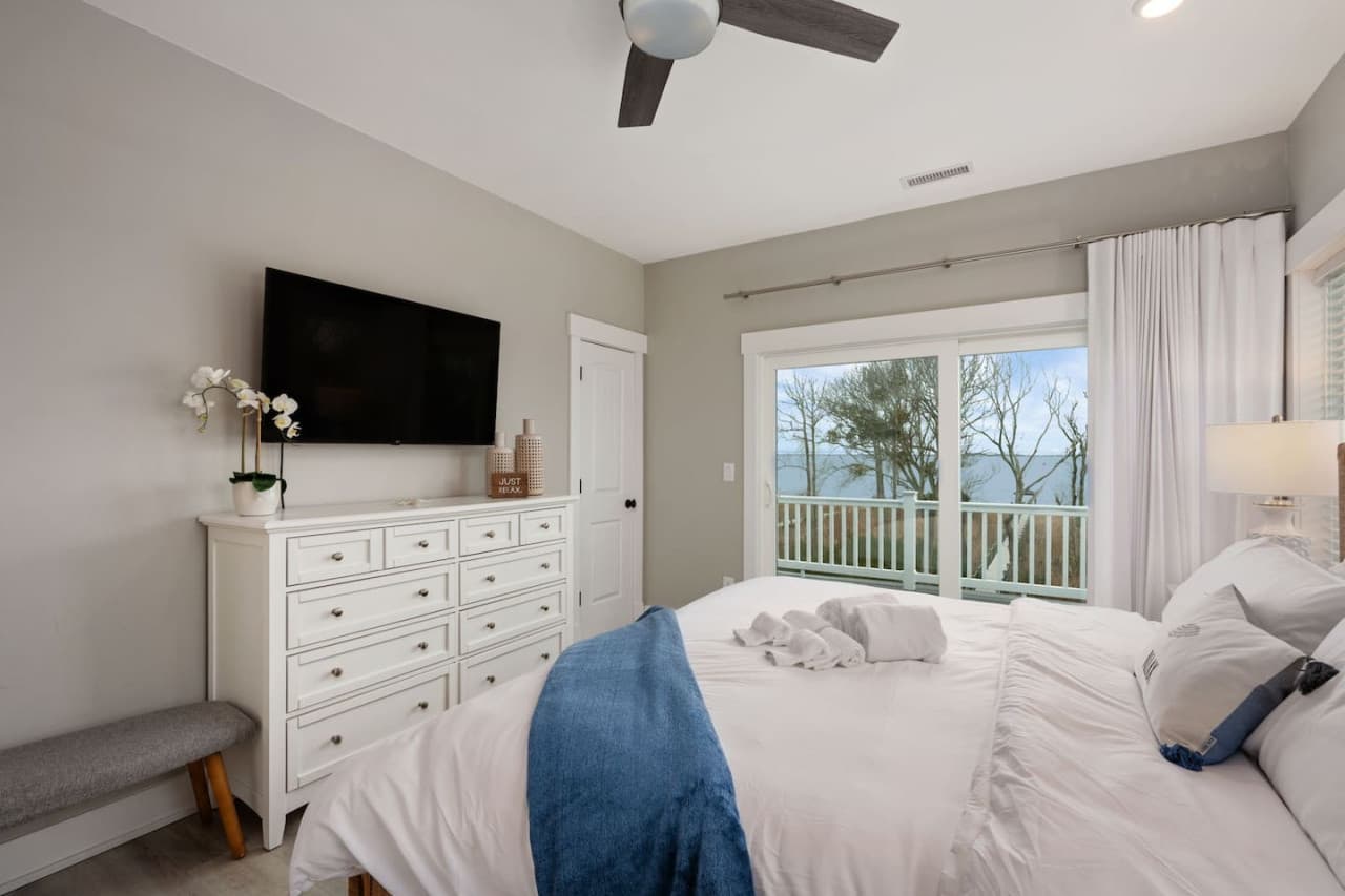 Relaxing bedroom setup w/ TV, dresser storage & views through sunlit windows.