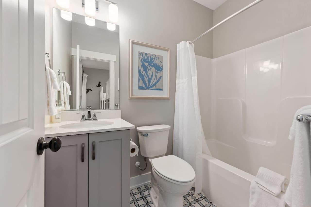 Clean bathroom w/ tub-shower combo, soft lighting & fresh coastal style.