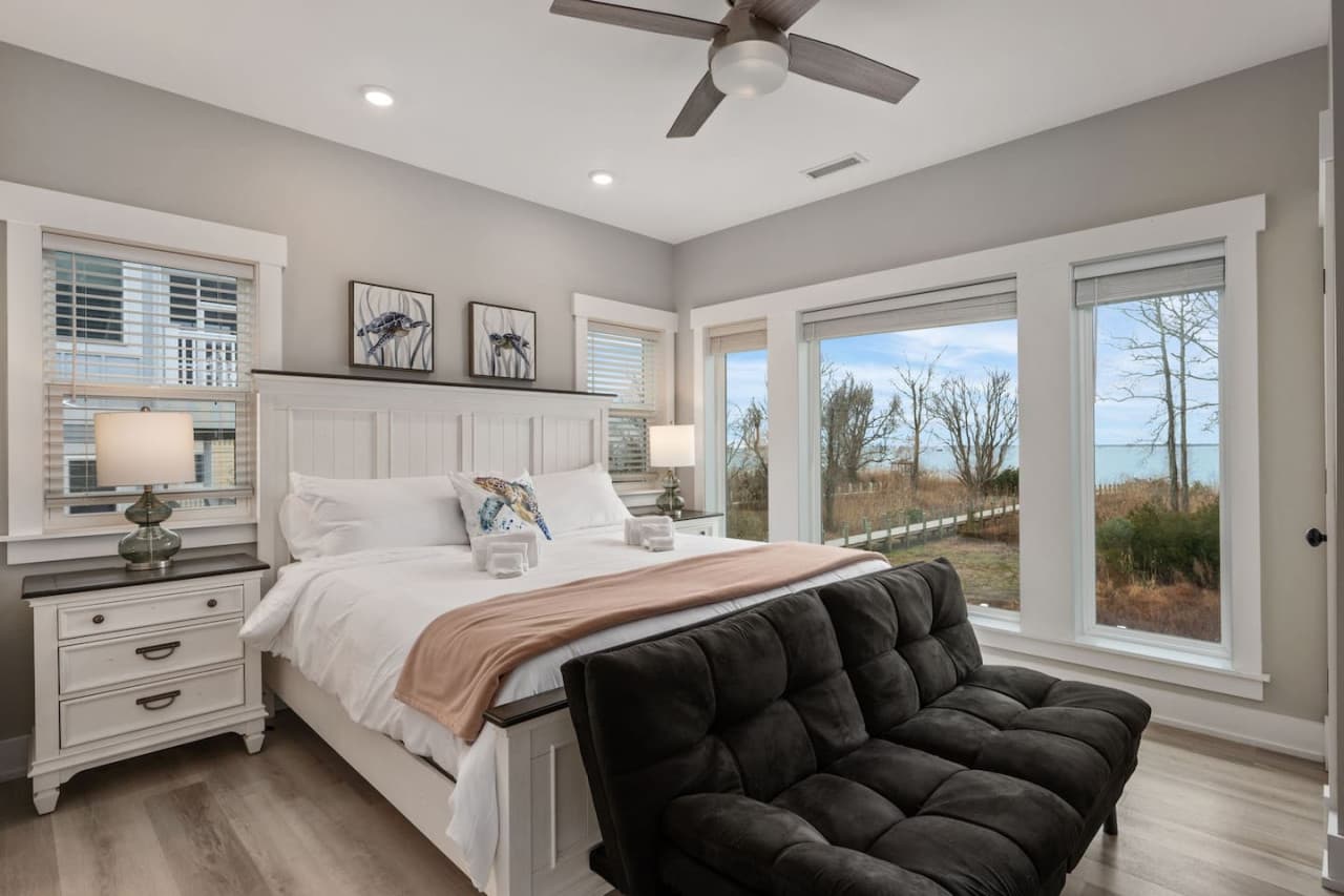 Airy bedroom w/ vaulted ceiling, tufted bench at the foot of the bed & sound views.