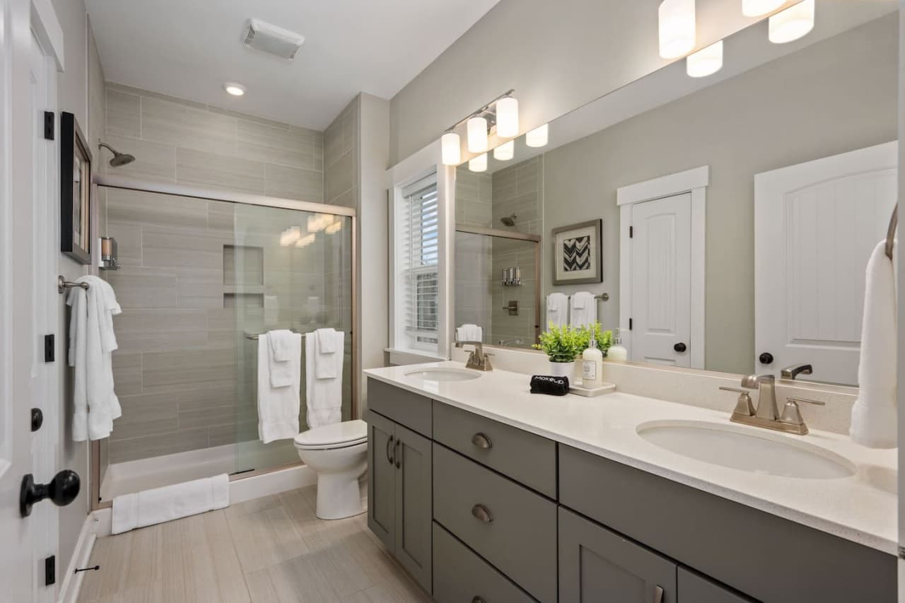 Shared bath w/ double vanity, wide mirror & a glass-door tub shower stocked w/ towels.