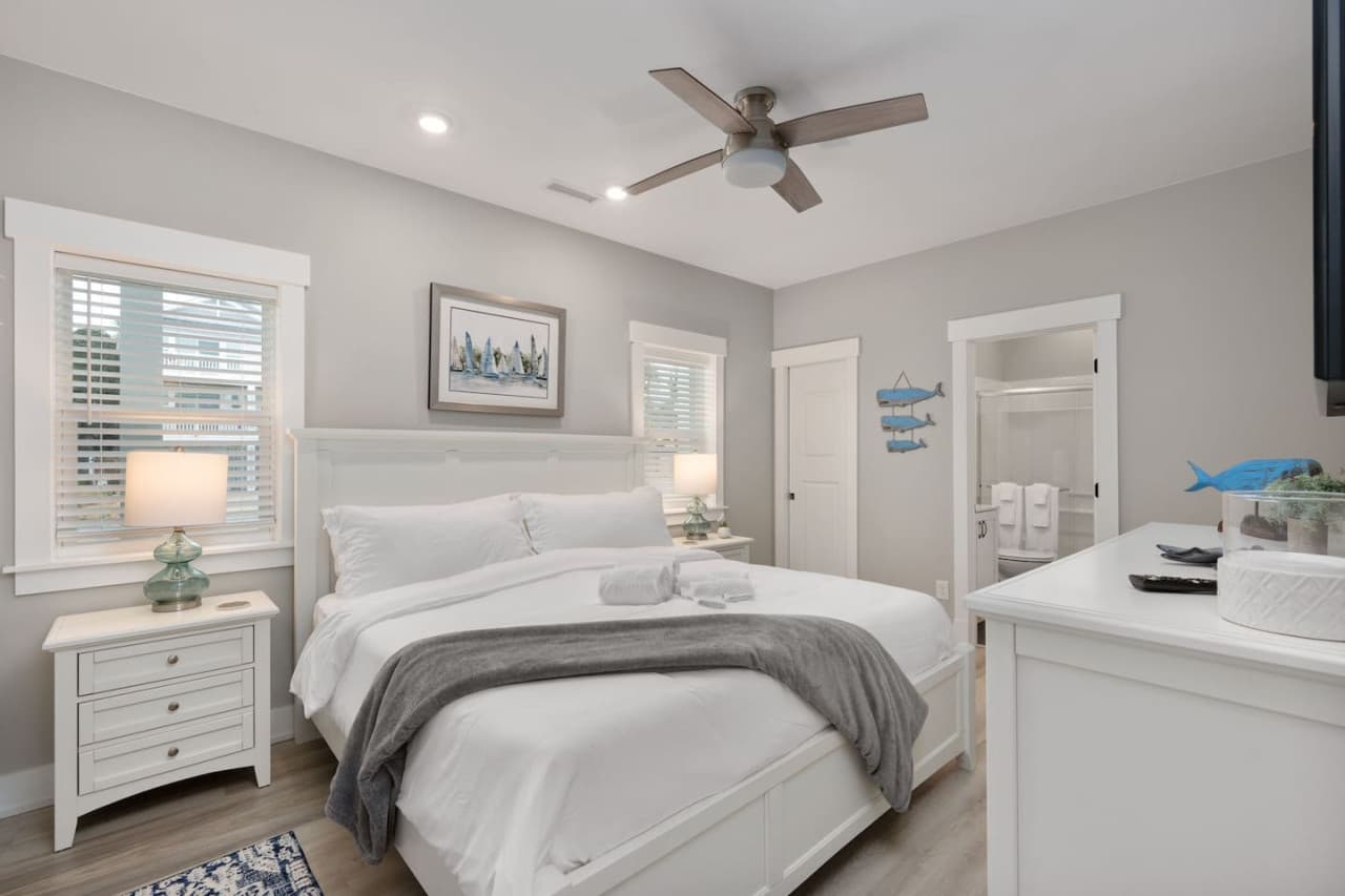 Bedroom w/ upholstered headboard, painted fish wall art & an ensuite bath through the door.
