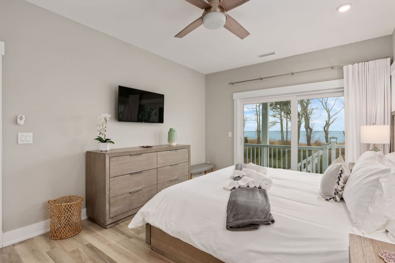 Bedroom w/ wood dresser, mounted TV & a slider to the deck overlooking the sound.