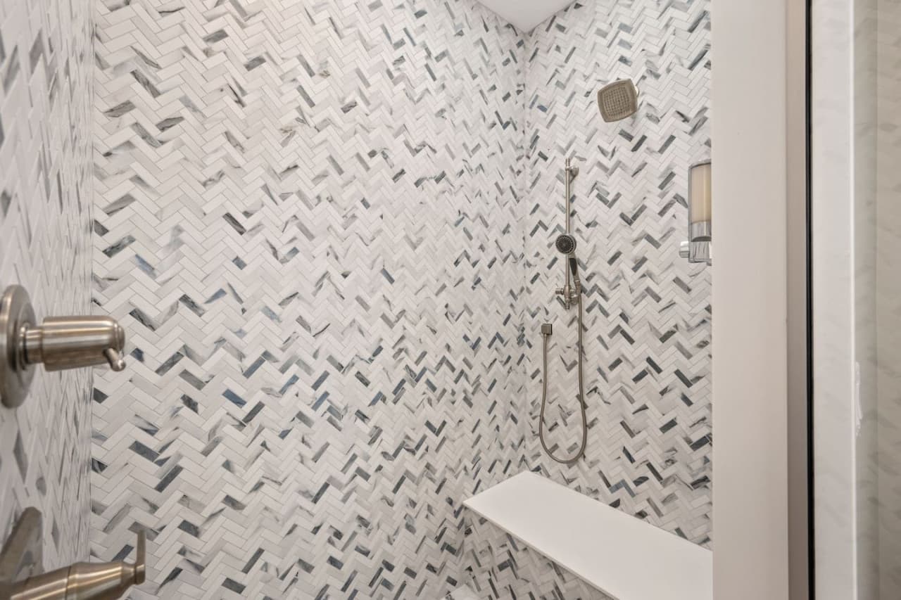 Walk-in shower detail w/ herringbone mosaic tile, built-in bench & handheld sprayer.