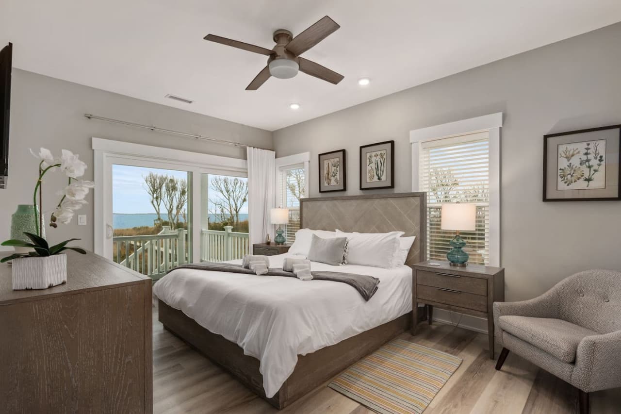 Bedroom w/ sound views through the windows, accent chair & ceiling fan overhead.