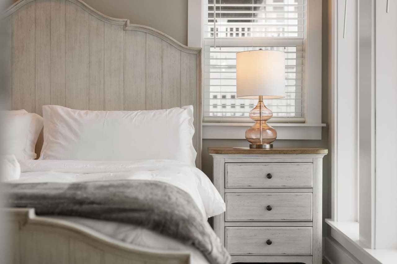Bedside detail w/ arched wood headboard, faux fur throw & a warm nightstand lamp.