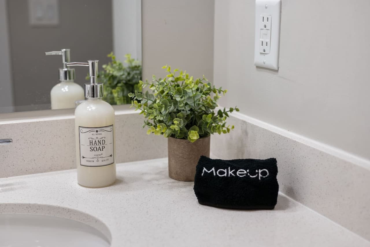 Vanity detail w/ hand soap, fresh greenery & a black makeup towel set out.