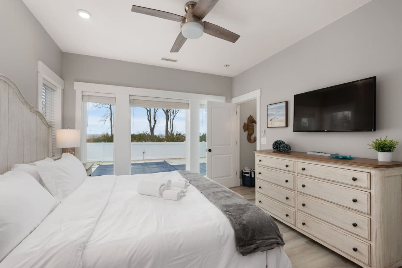 Bedroom w/ mounted TV, wide dresser & French doors opening onto the pool deck.