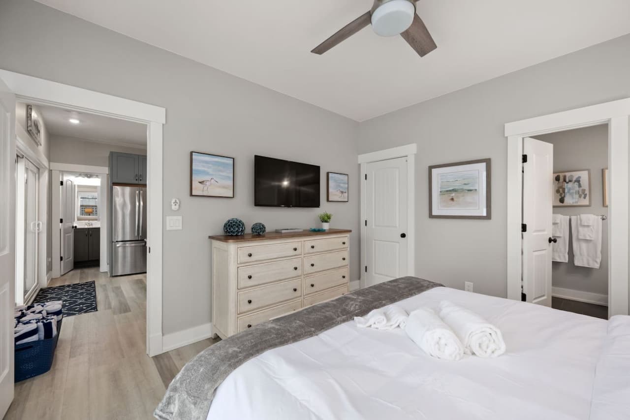 Bedroom w/ mounted TV, white dresser & an ensuite bath right off the room.