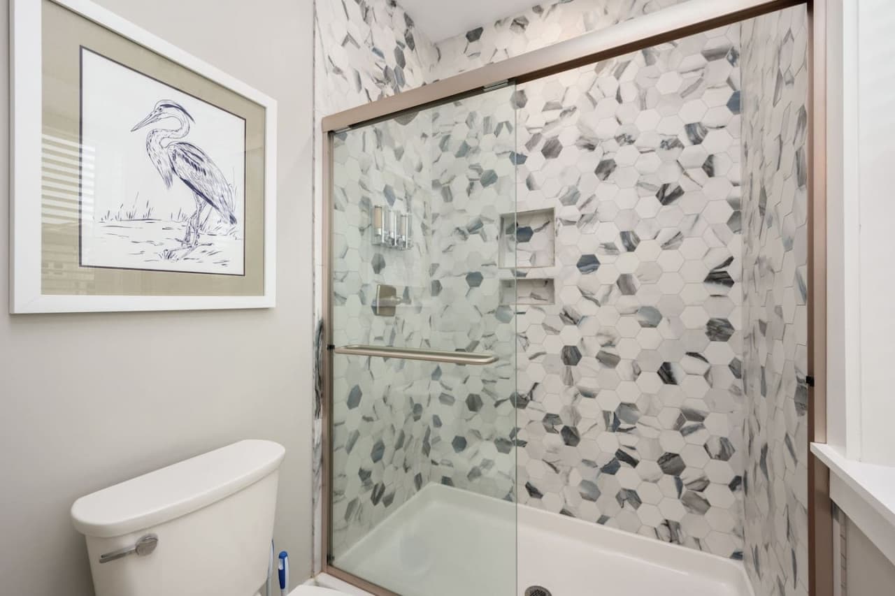 Bath w/ pebble-tile tub shower, heron print & a light, breezy coastal feel.