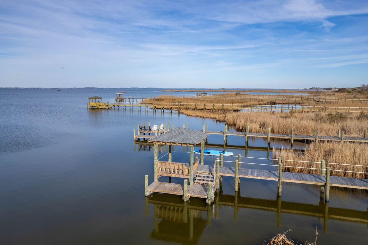 Wide open sound water w/ weathered docks lining the marsh grass along the shoreline.