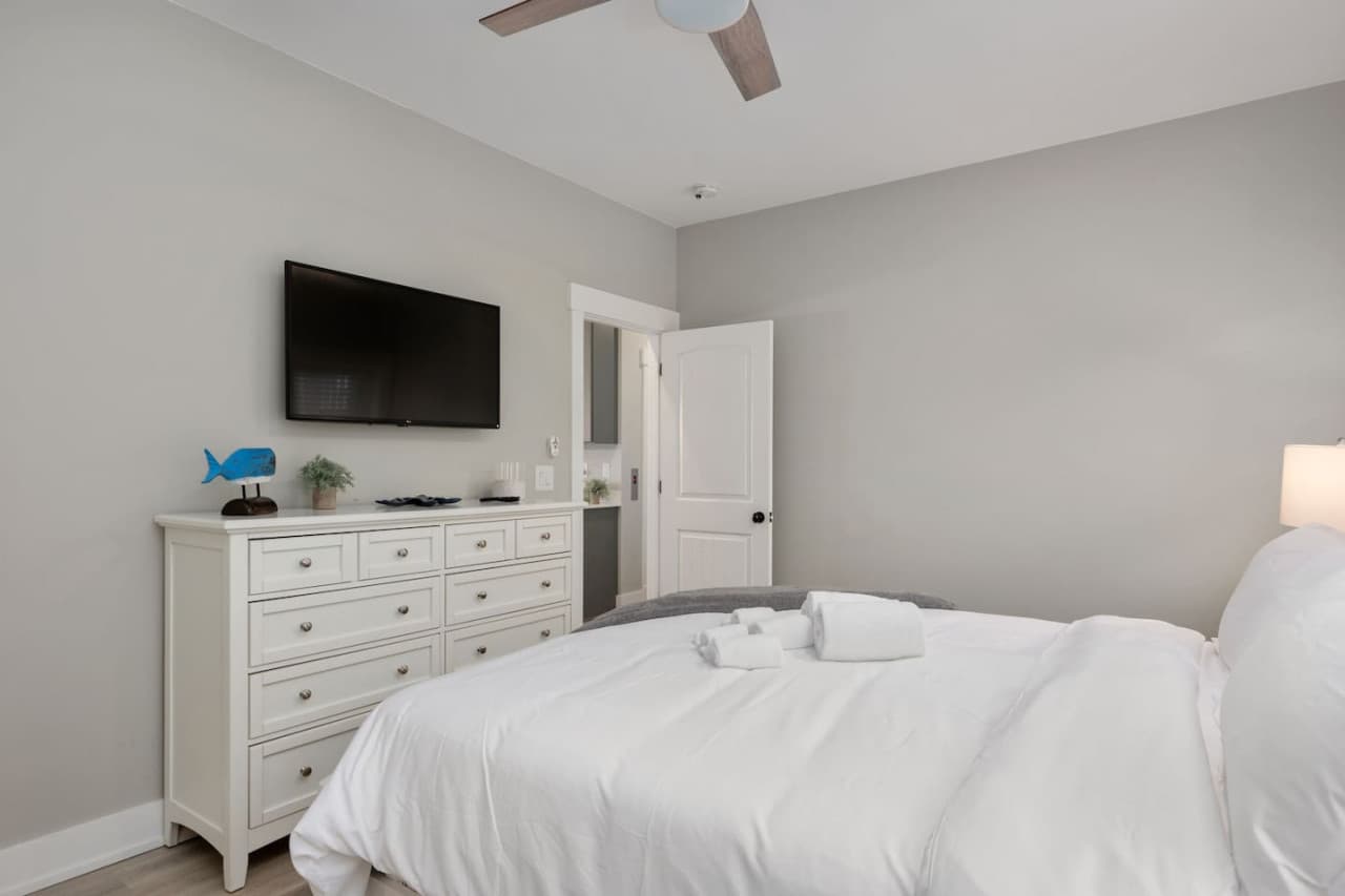 Simple, restful bedroom w/ mounted TV, white dresser & ensuite bath alongside.