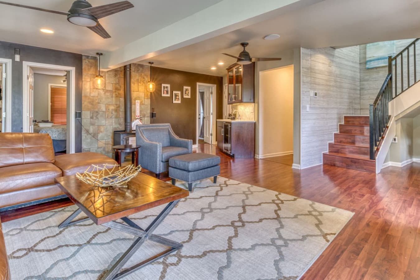 Second Floor Media Room features a large sectional with 70inch Smart TV, wood-burning stove, wet bar with marvel wine fridge, workspace with desk and chair, access to 2nd-floor bedrooms and full bathroom, and East Deck overlooking the National Park