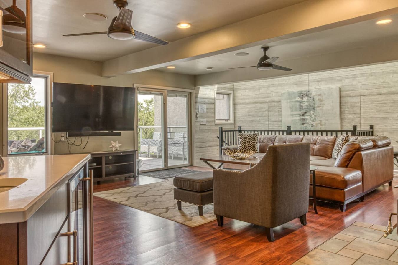Second Floor Media Room features a large sectional with 70inch Smart TV, wood-burning stove, wet bar with marvel wine fridge, workspace with desk and chair, access to 2nd-floor bedrooms and full bathroom, and East Deck overlooking the National Park