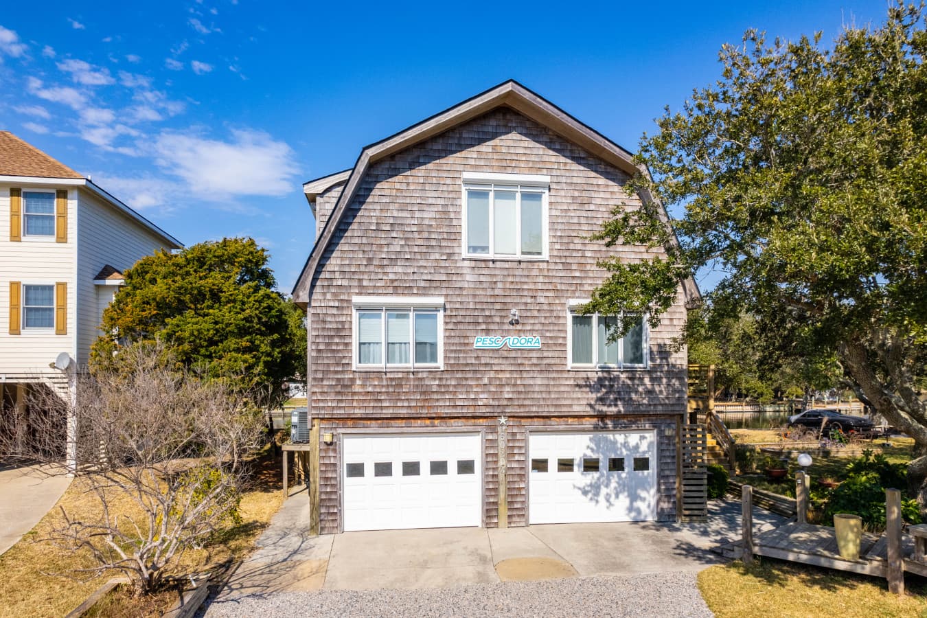 Welcoming home exterior w/ classic coastal charm, framed by greenery & a sunny blue sky.
