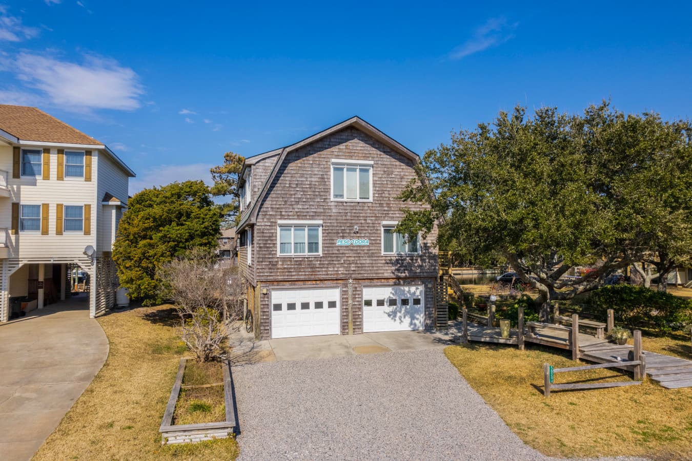 Charming home exterior w/ classic coastal style, framed by trees and bright blue skies.
