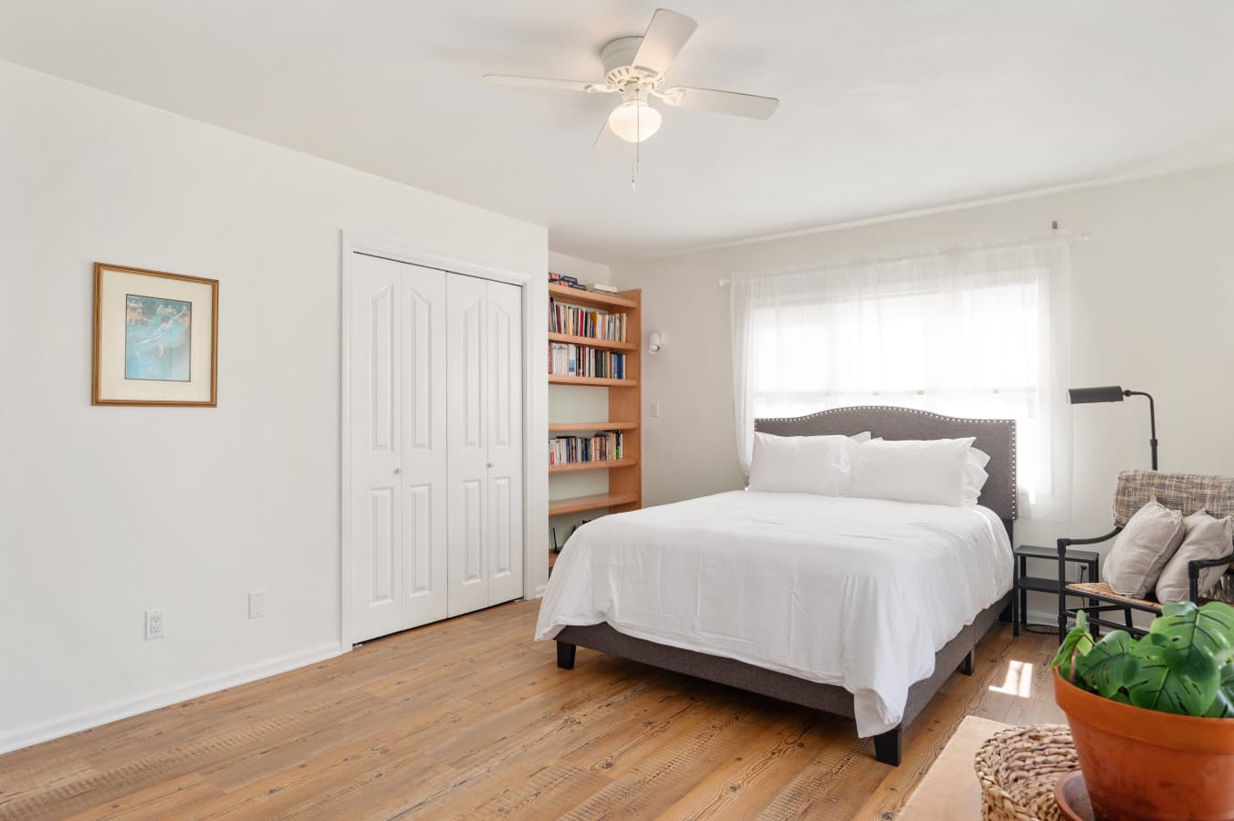 Bright bedroom w/ comfy bed, soft linens, & natural light pouring through sheer curtains.