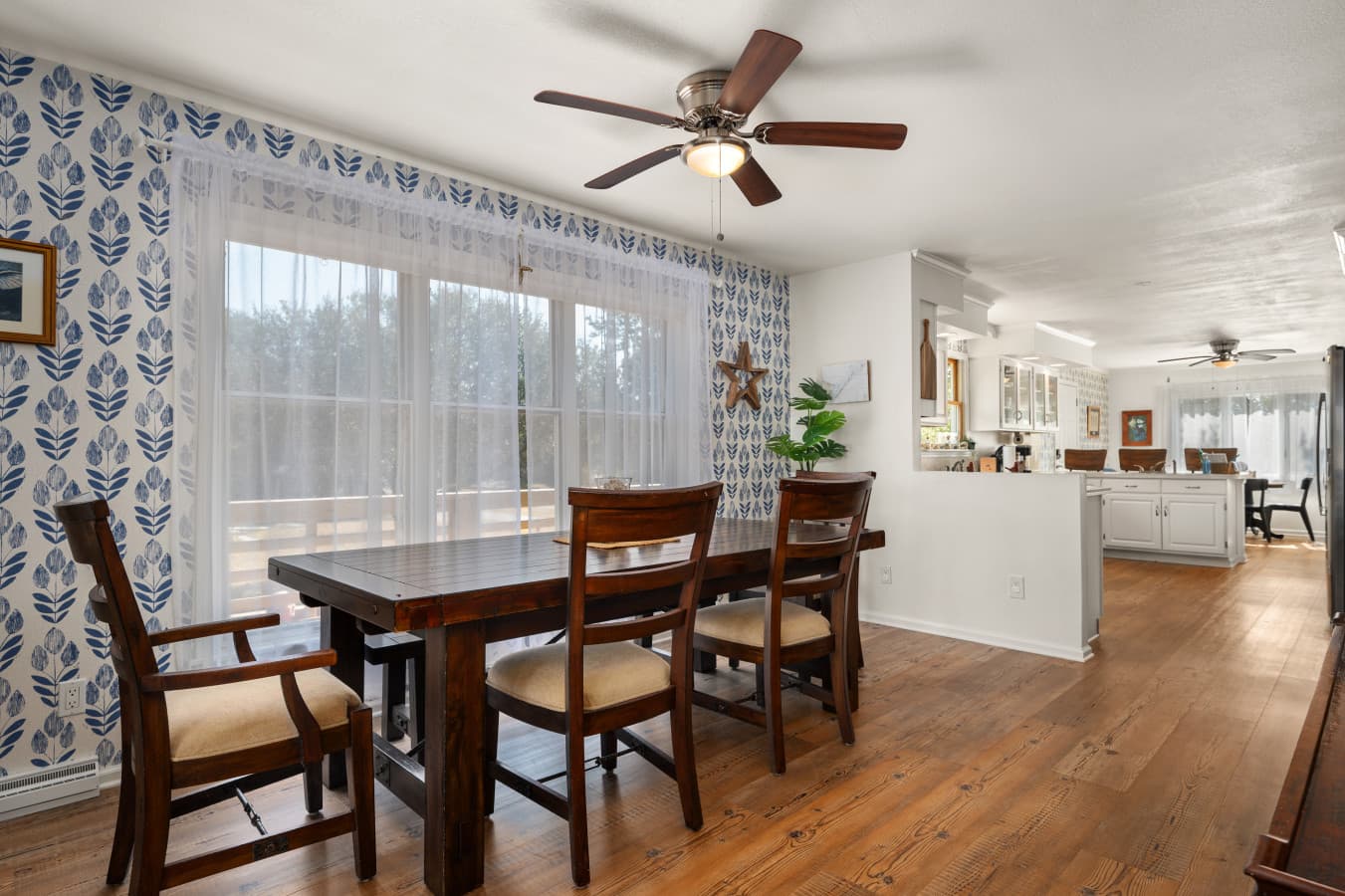 Sunlit dining nook w/ wood table beside large windows and easy flow to the kitchen.