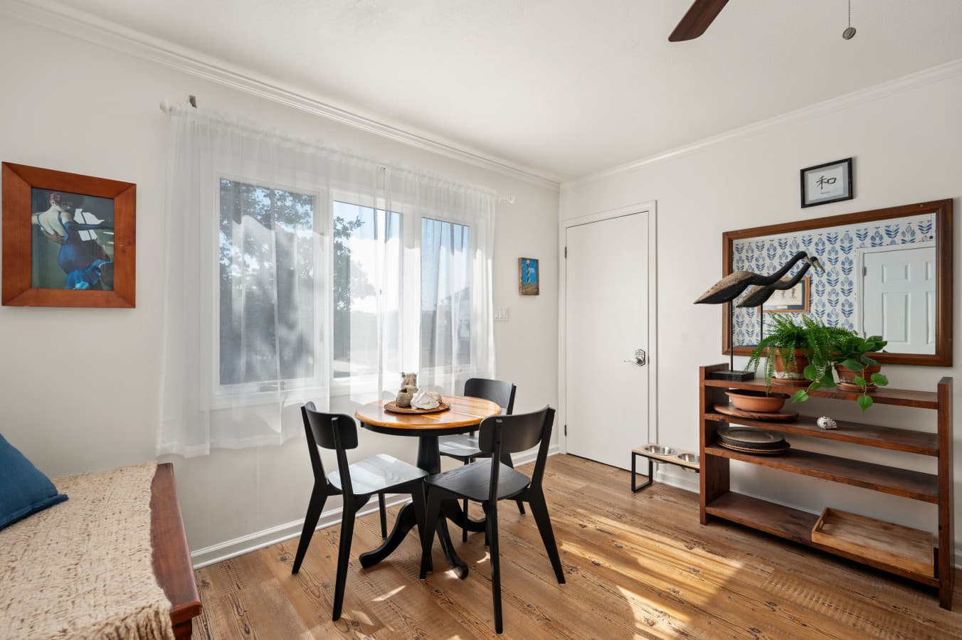 Breakfast nook w/ round table, two chairs & open wood shelving beside a sunny window.