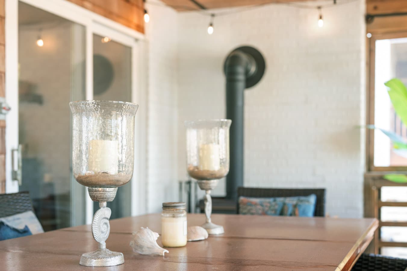 Porch table detail w/ hurricane candles & shells, set for unhurried evenings outside.