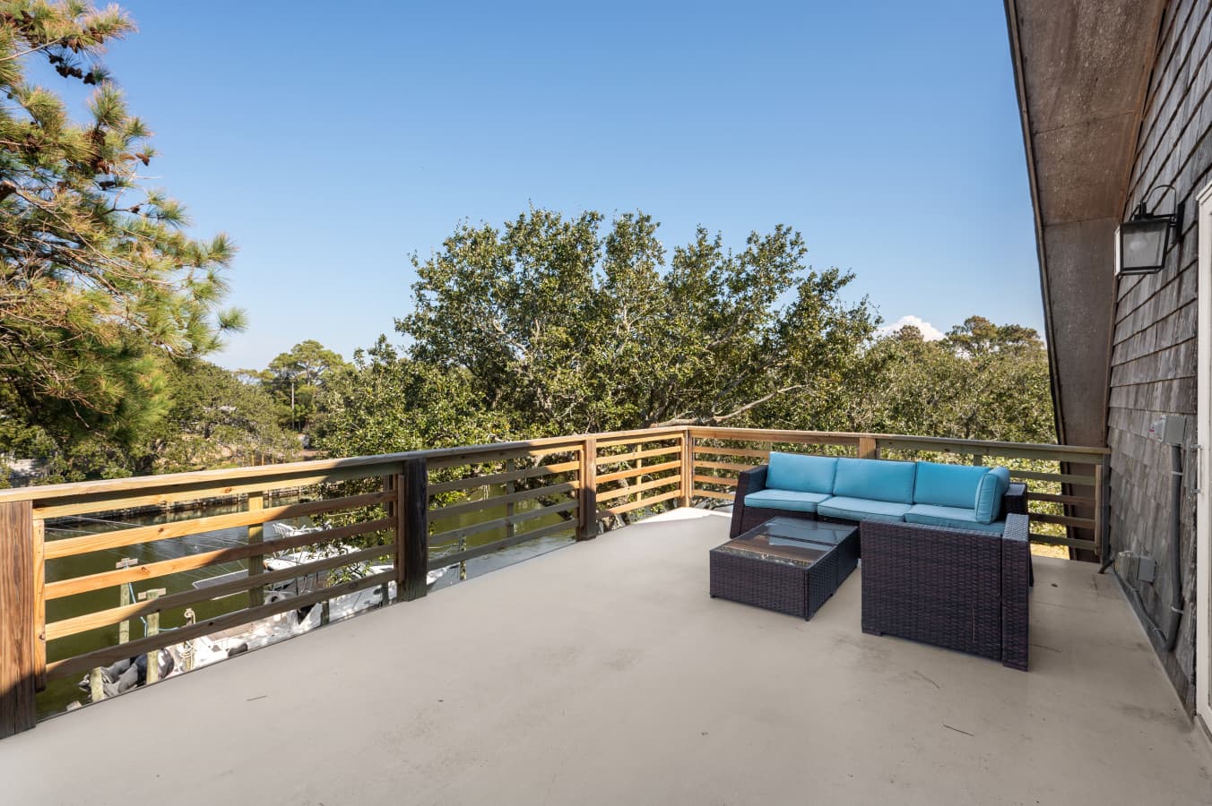 Sun deck w/ cushioned wicker sectional & wood railing, framed by treetops for quiet afternoons.
