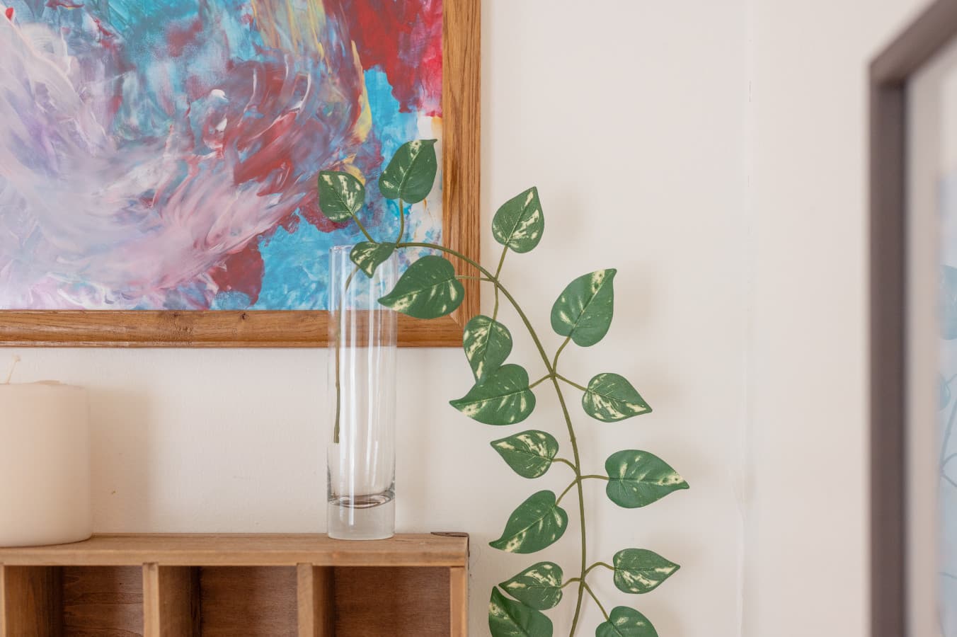 Decor detail w/ abstract art above a wood console & a slim vase of greenery.