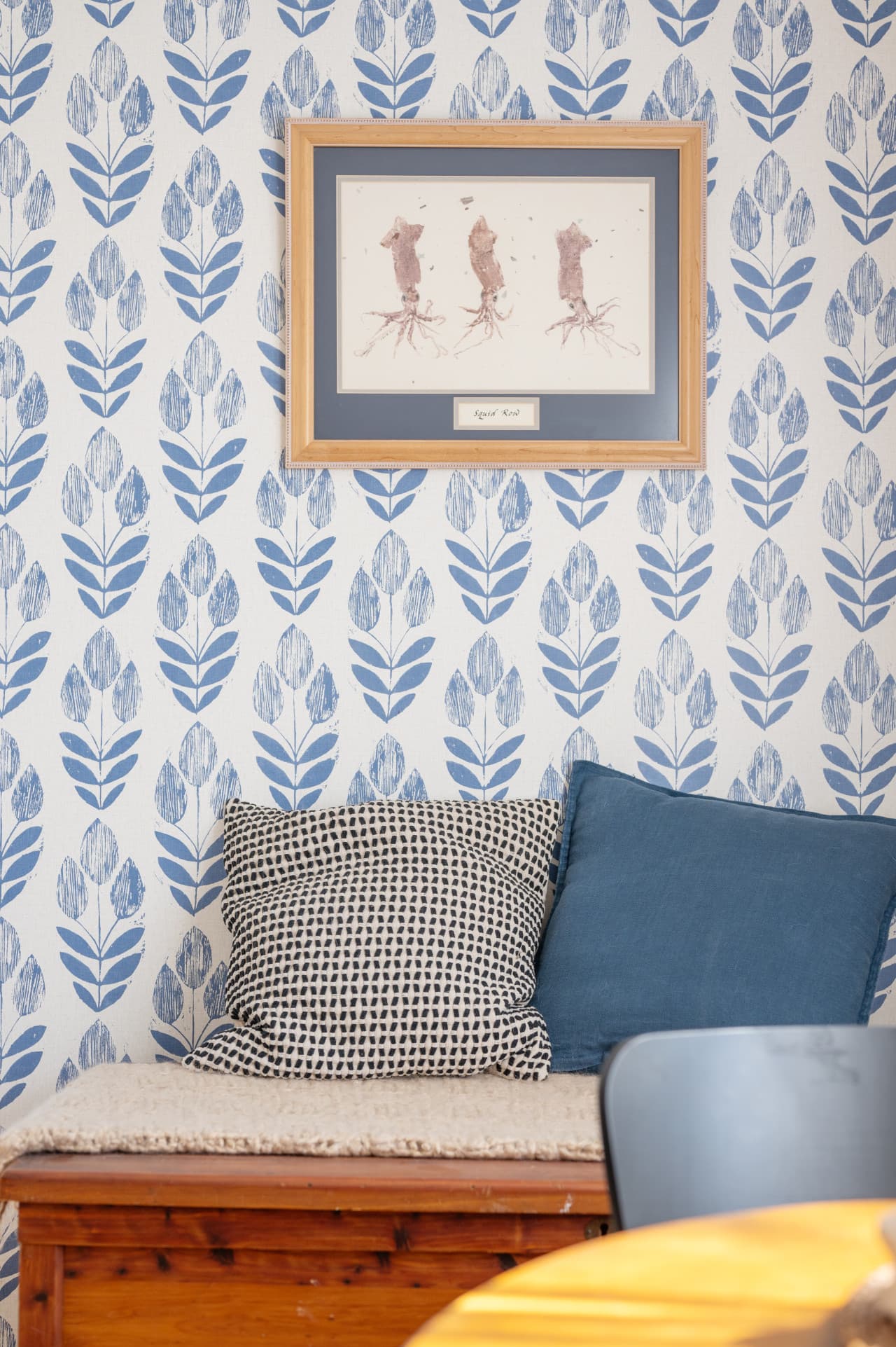 Cushioned window bench w/ blue botanical wallpaper & framed art, a quiet spot to read.