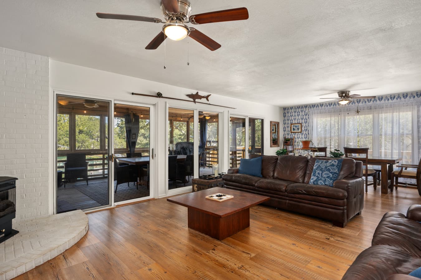 Open living room w/ leather sofas, ceiling fan & a wall of glass doors to the porch beyond.