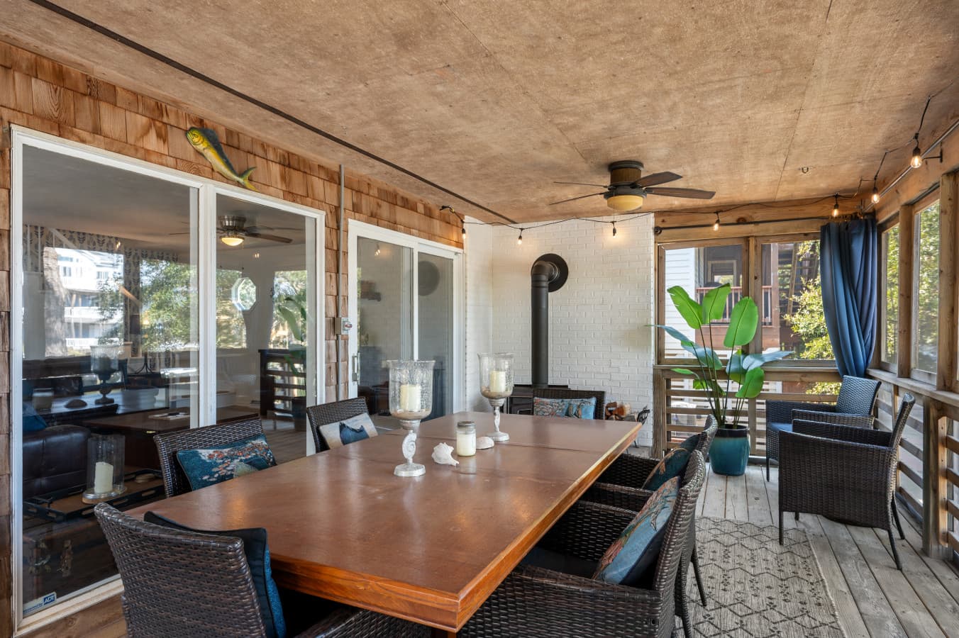 Screened porch w/ long dining table, wicker chairs, string lights & a wood stove for cool nights.