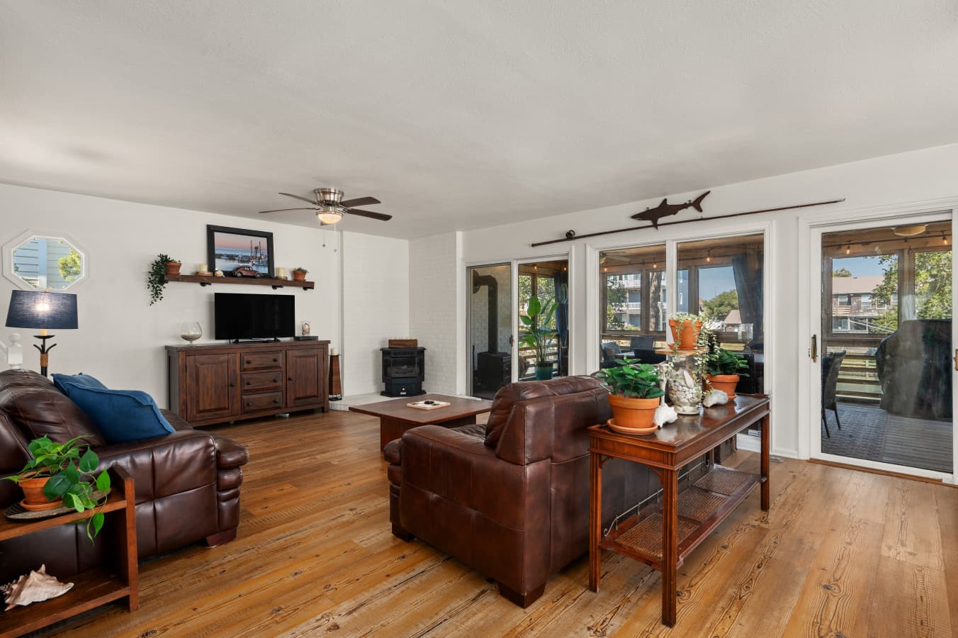 Living room w/ leather seating, wood floors & a wall of glass doors framing the porch.
