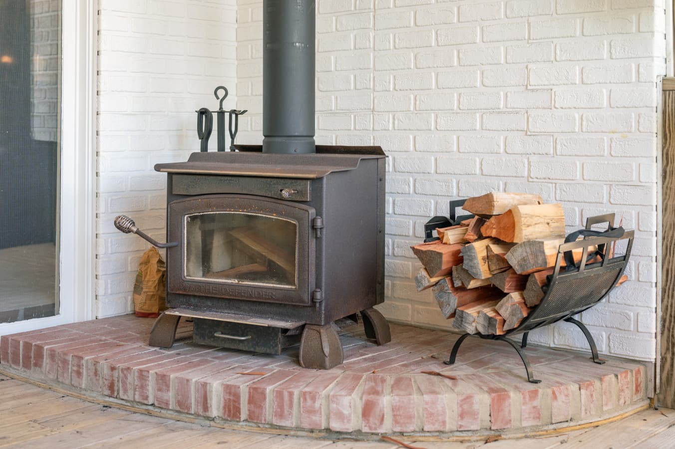 Wood-burning stove on a brick hearth w/ split firewood ready for chilly evenings.