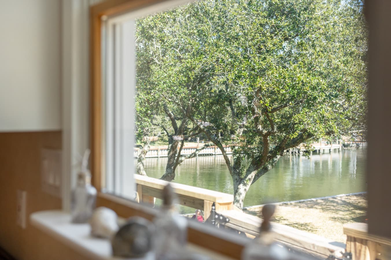 Window view over the canal & a wide live oak, w/ small figurines lined up on the sill.