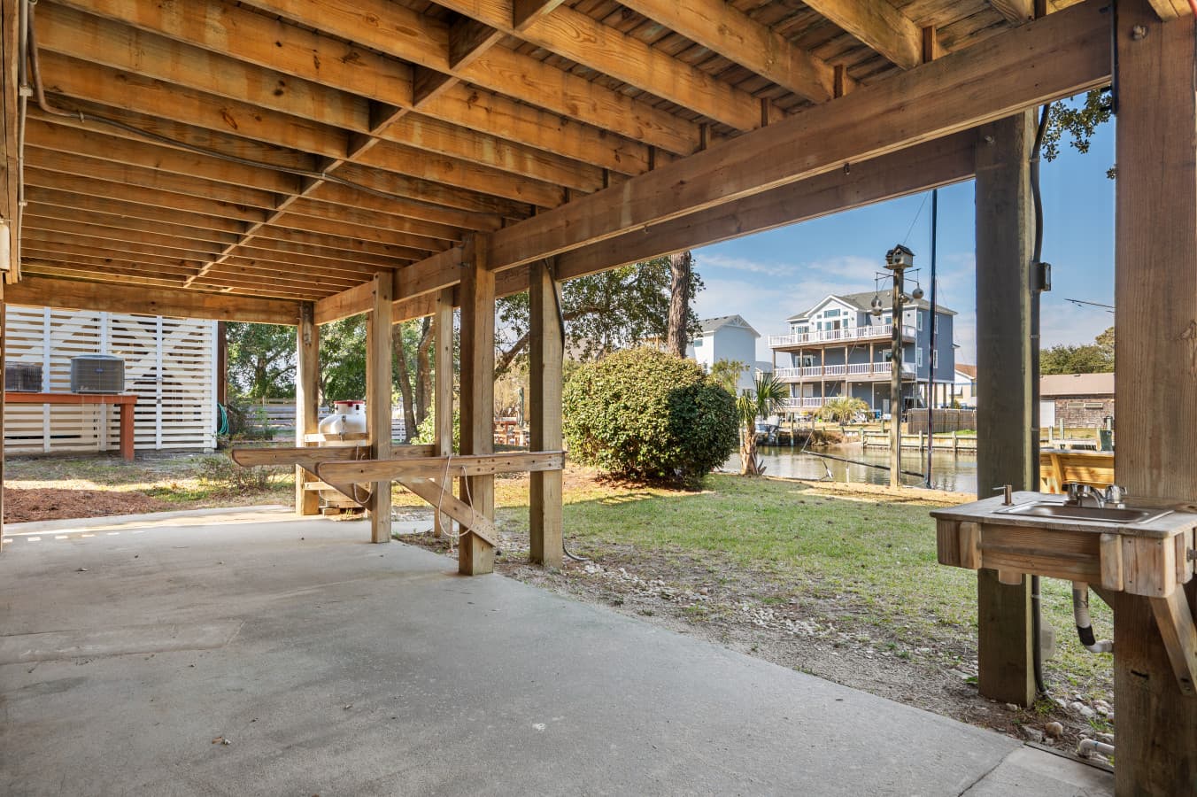 Covered parking beneath the house w/ a bench & open yard just beyond.