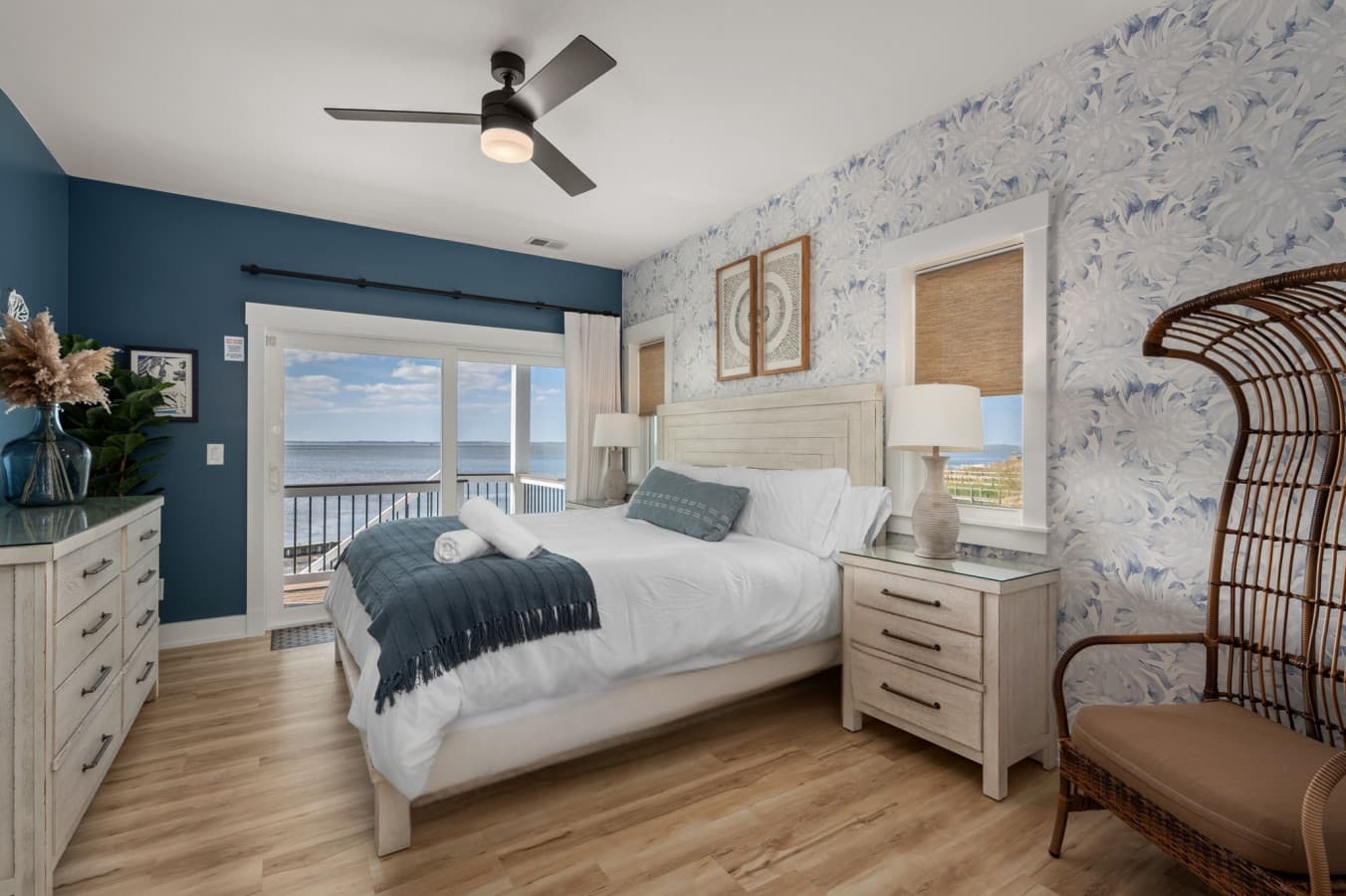 Serene bedroom w/ a cozy bed, soft coastal tones, & glass doors opening to a private balcony w/ calming water views.