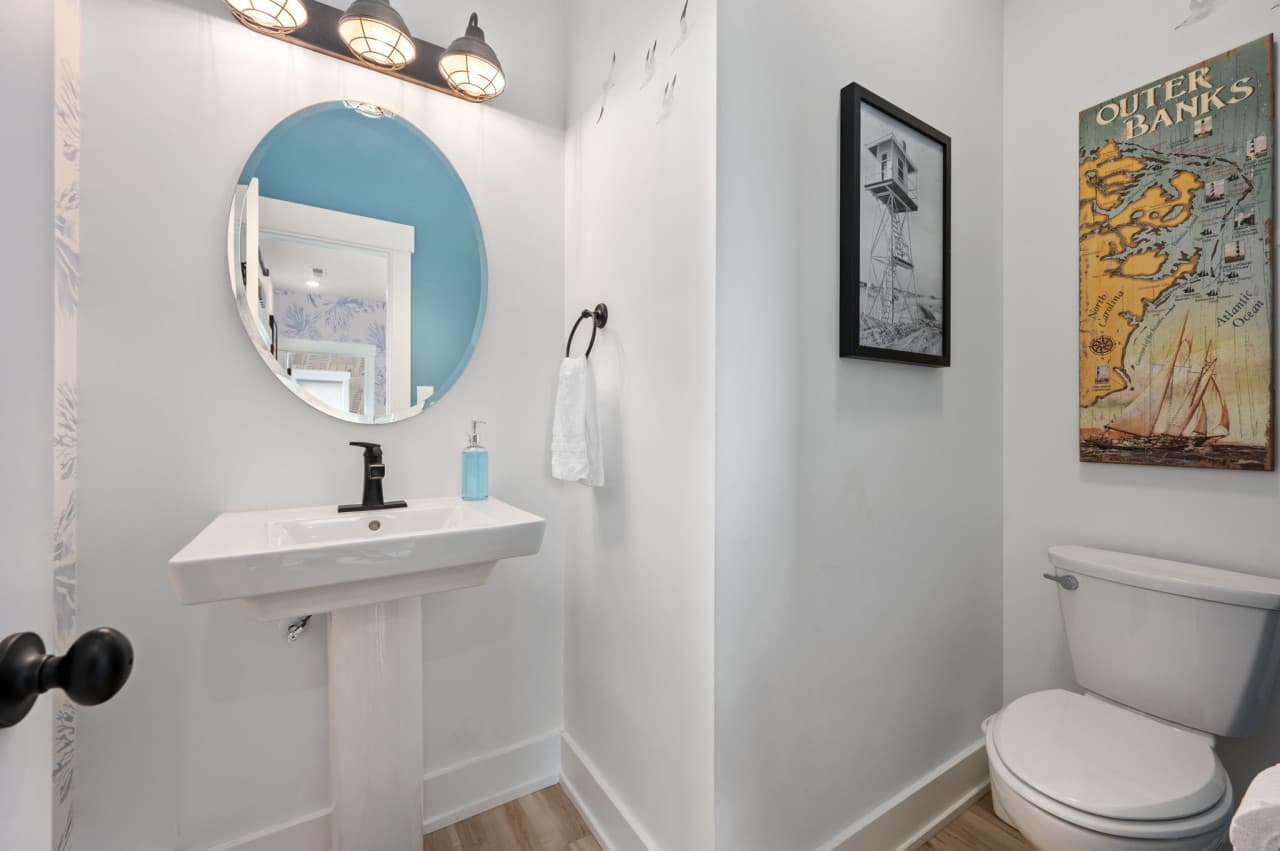 Clean powder bath w/ pedestal sink, round mirror & simple coastal charm.