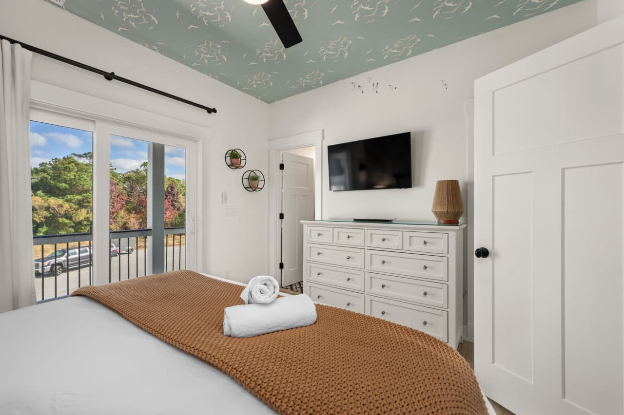 Bright bedroom w/ TV, dresser & doors that open to outdoor light.