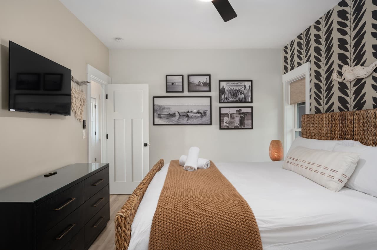 Long bedroom w/ soft neutrals, wall-mounted TV & a calm layout designed for unwinding.