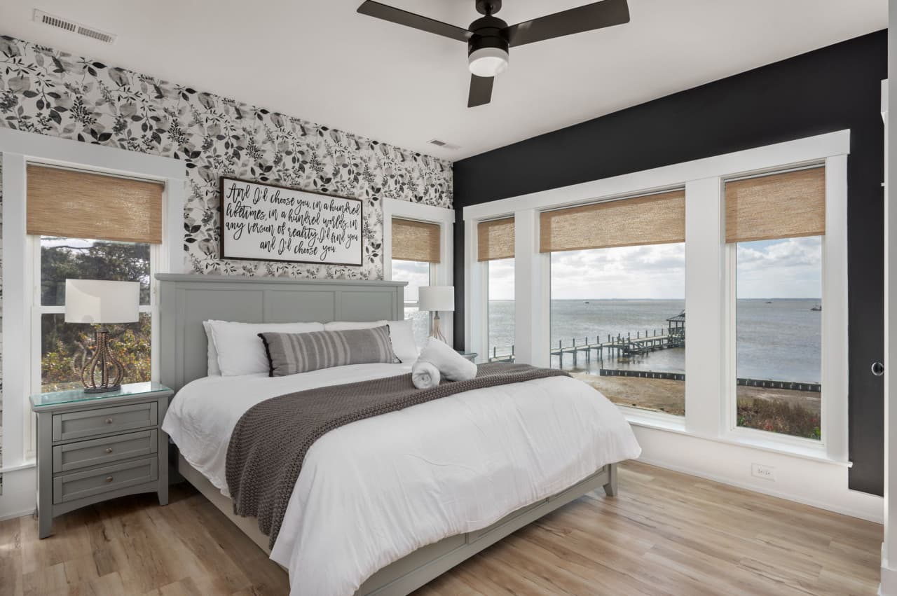 Sunlit bedroom w/ patterned accent wall, plush bedding & large windows that brighten the space.