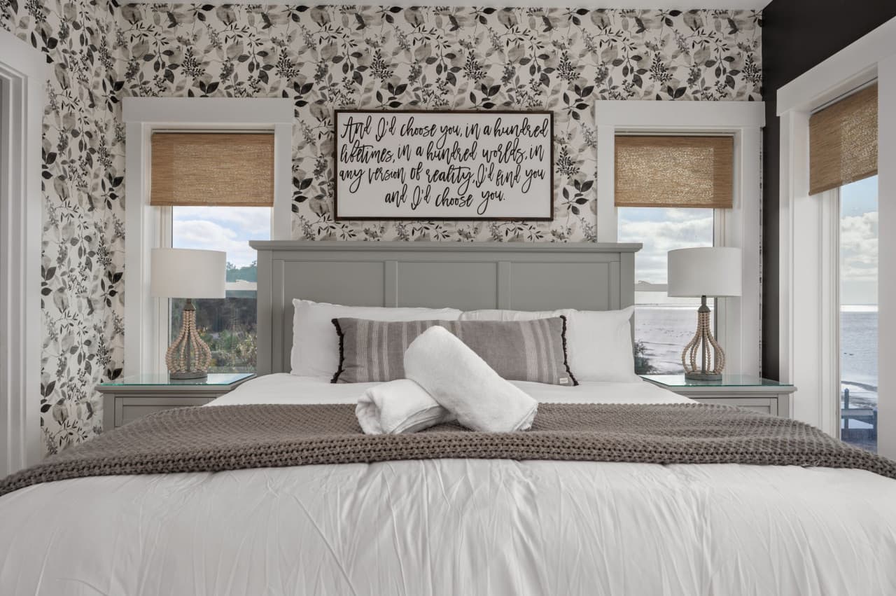 Bedroom w/ soft patterned wallpaper, a padded headboard & bedside lamps for easy nights.