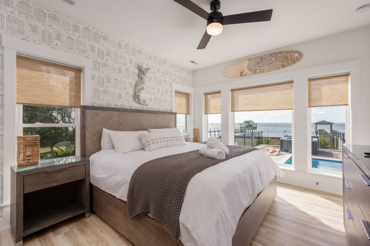 Bedroom w/ a herringbone headboard & windows over the pool and the sound beyond.