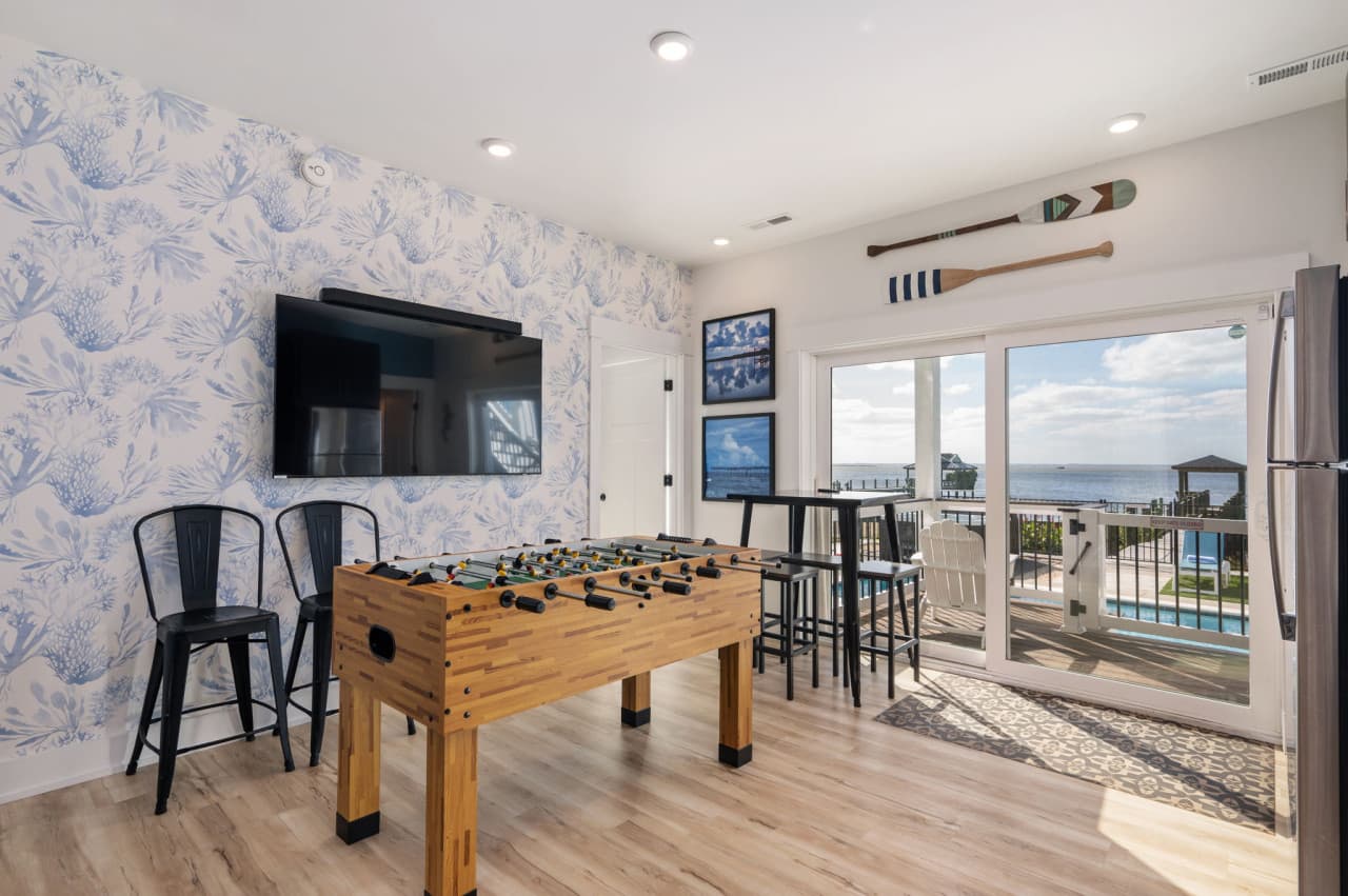 Game room w/ a foosball table, wall TV & bar seating, opening straight out to the deck.