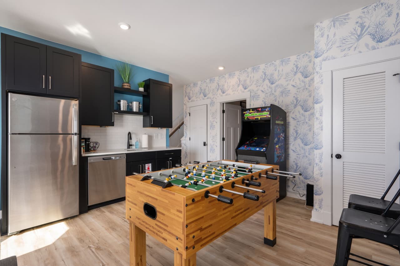 Kitchenette beside the game room w/ a full fridge, foosball table & an arcade machine.