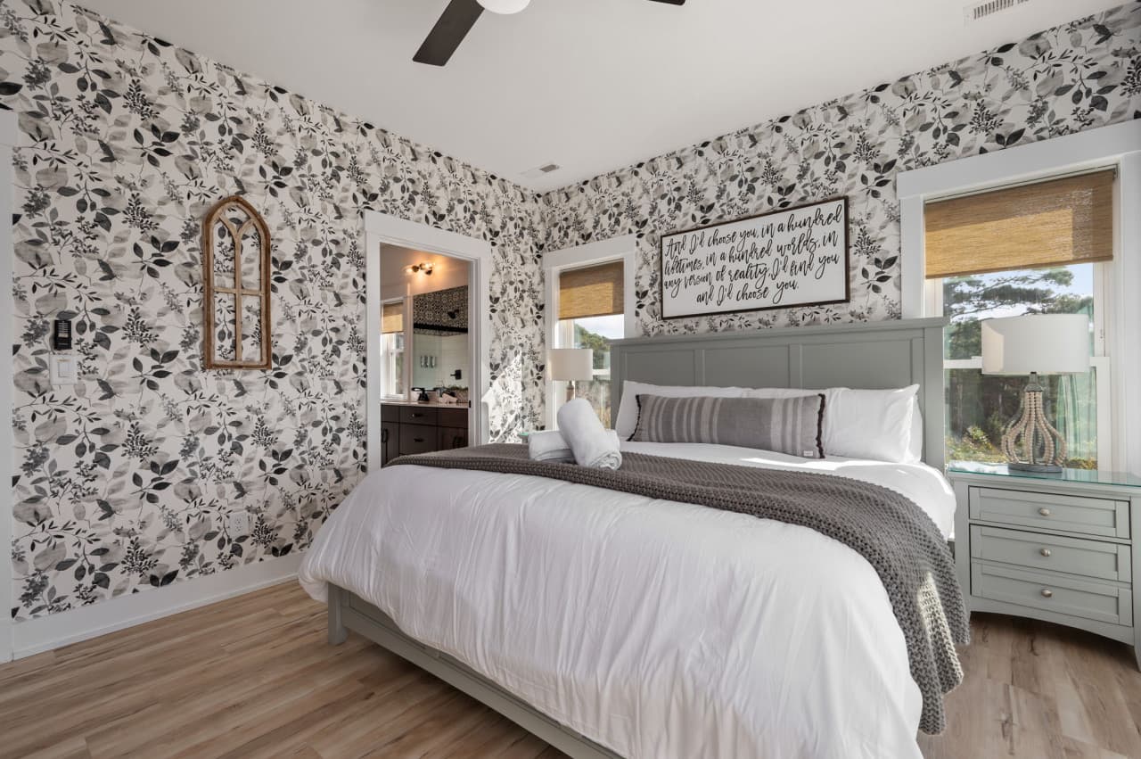 Bedroom w/ dark botanical wallpaper, framed script art & crisp white bedding.