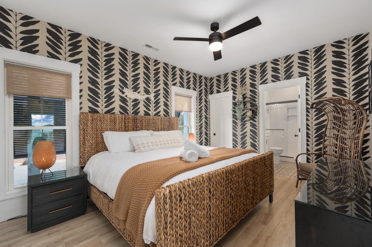 Bedroom w/ chevron wallpaper, a woven headboard & a ceiling fan for restful nights.