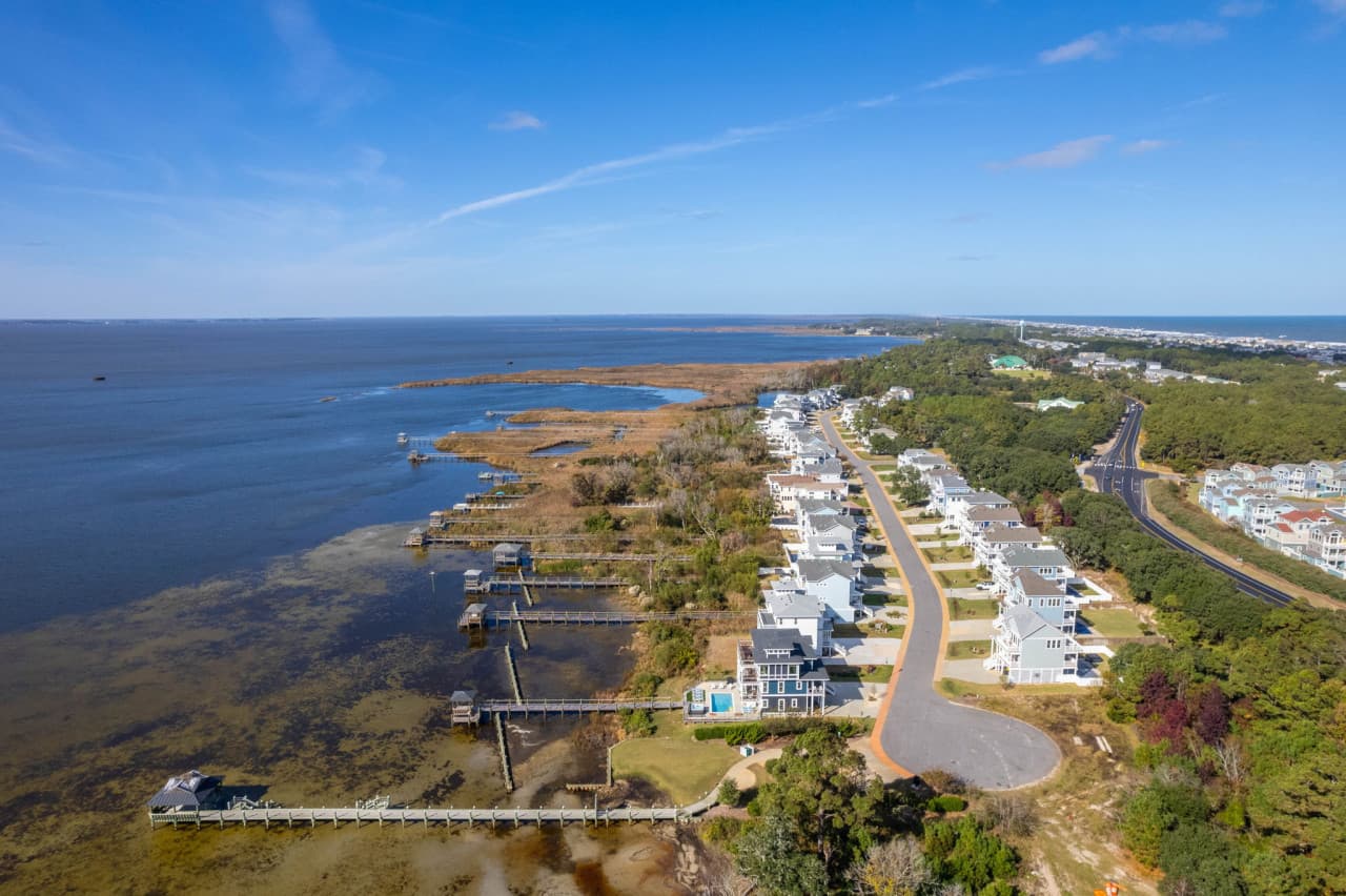 Aerial along the sound shoreline, homes and docks lining the water's edge.