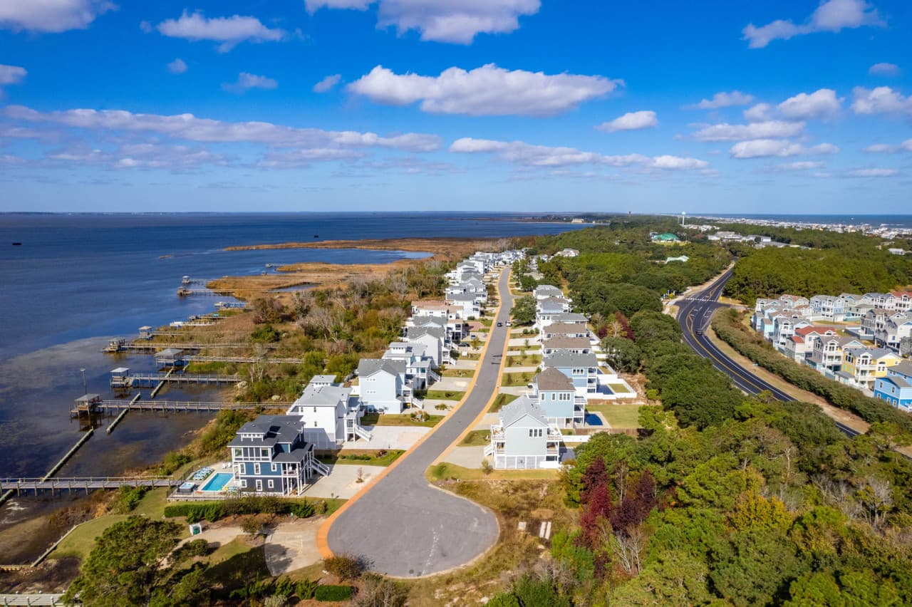 Aerial down the sound shoreline w/ homes, marsh & open water side by side.