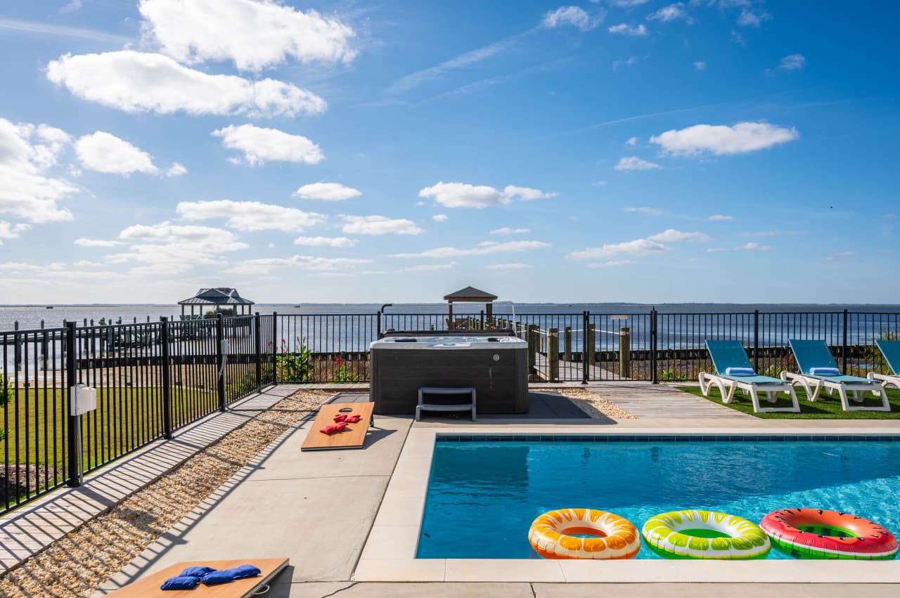 Pool deck w/ hot tub, cornhole boards & loungers lined up facing the sound.