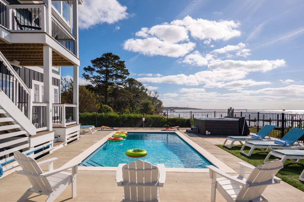 Pool & sun deck alongside the house w/ loungers, floats & the sound in the distance.
