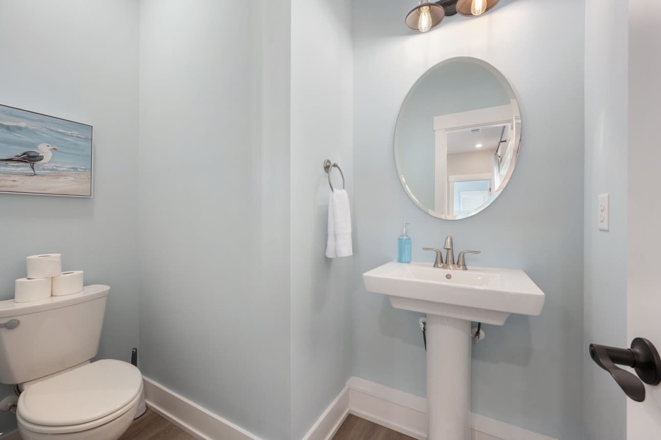 Tidy half bath w/ pedestal sink, round mirror & coastal art for quick guest stops