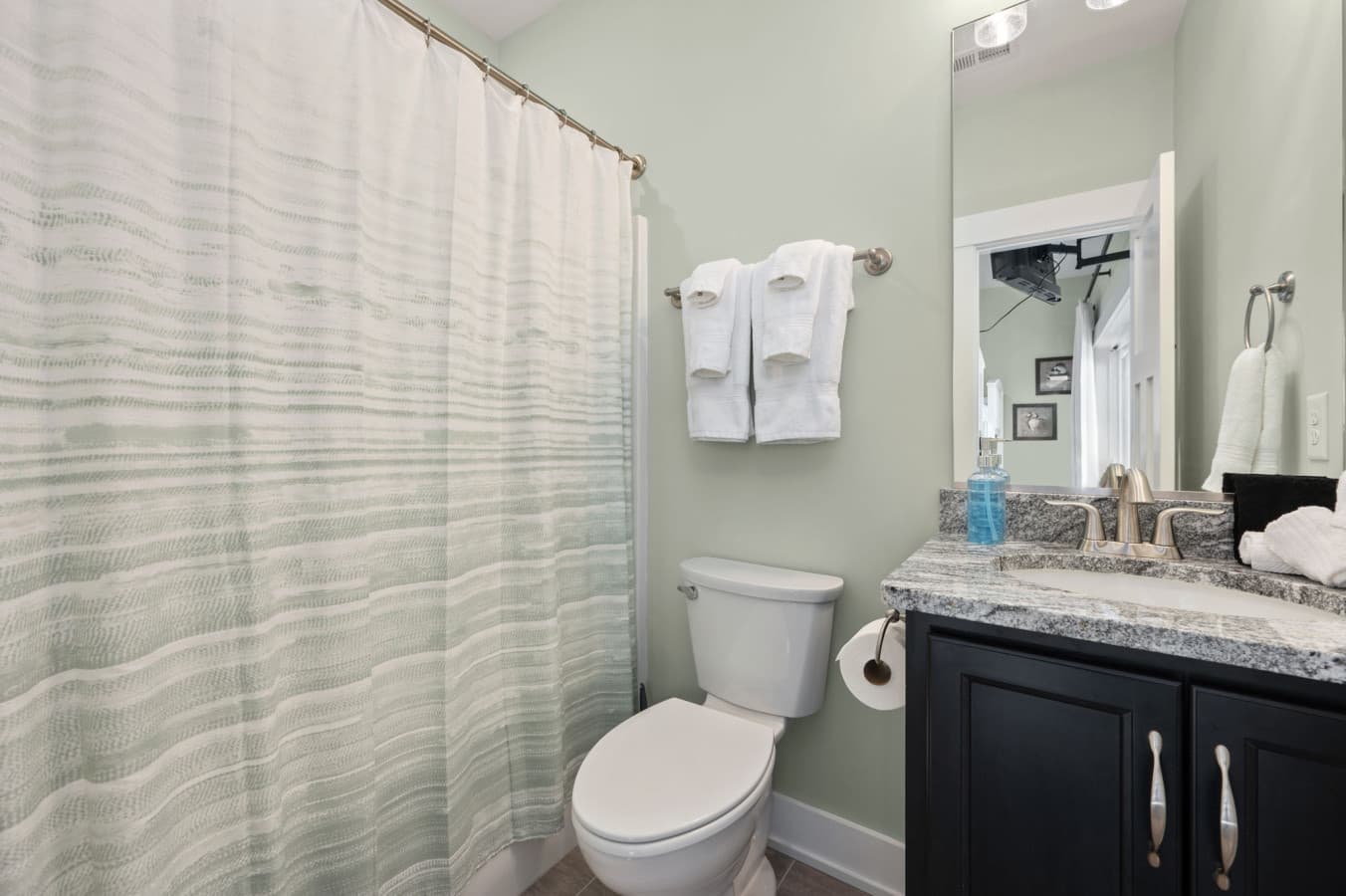 Full bath w/ dark vanity, granite counter & a tub-shower behind the curtain